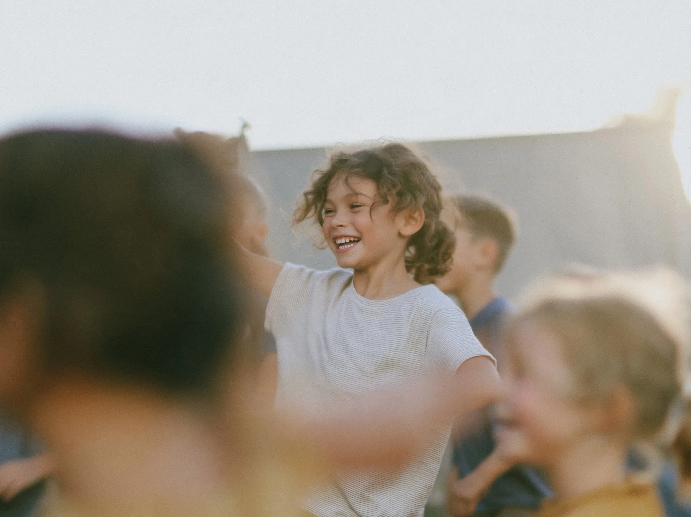 A laughing child in a striped T-shirt moving with a group of children, blurred with motion, in soft evening light.