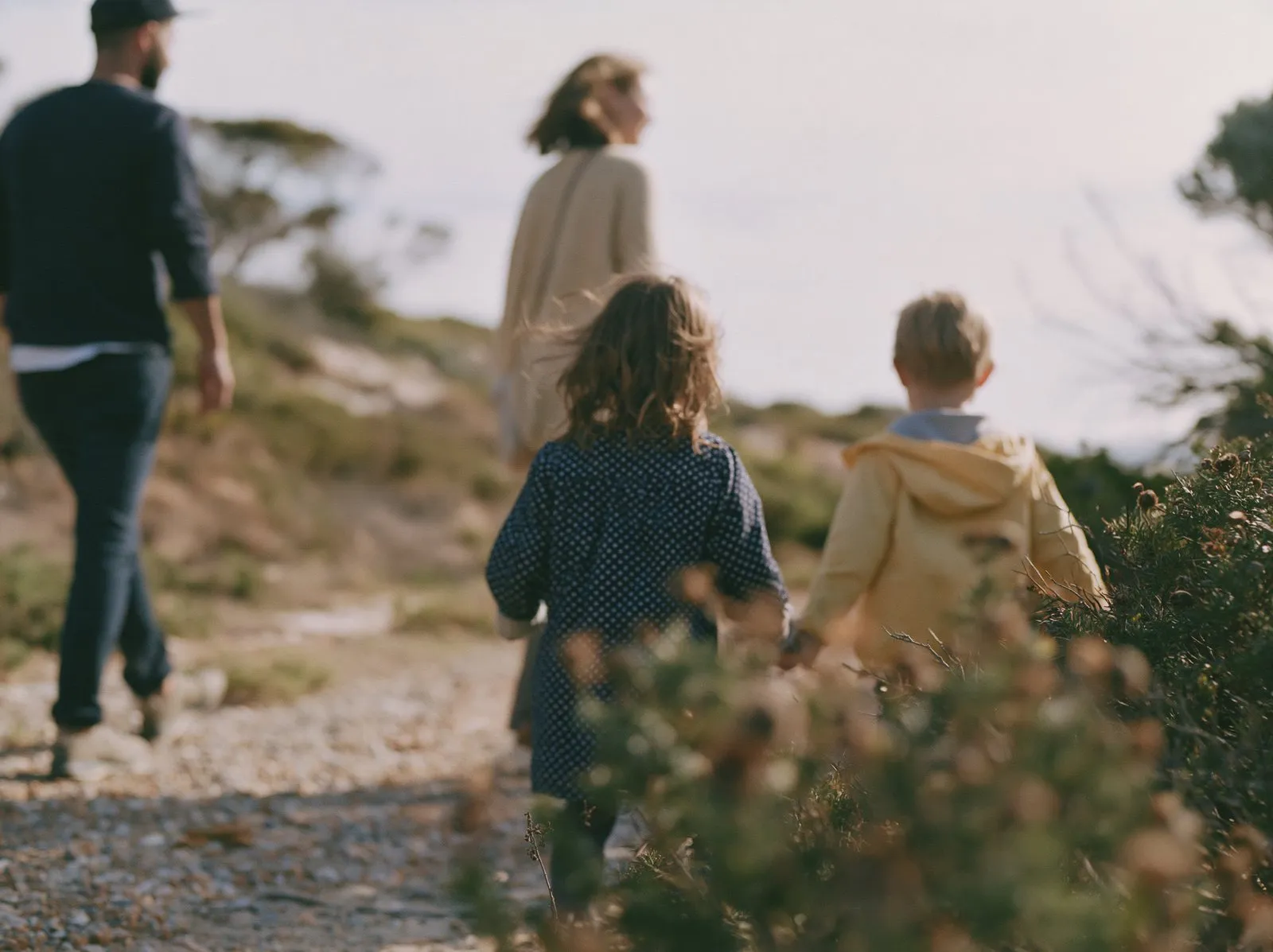 Two children and two adults walking along a gravel path through low scrub.