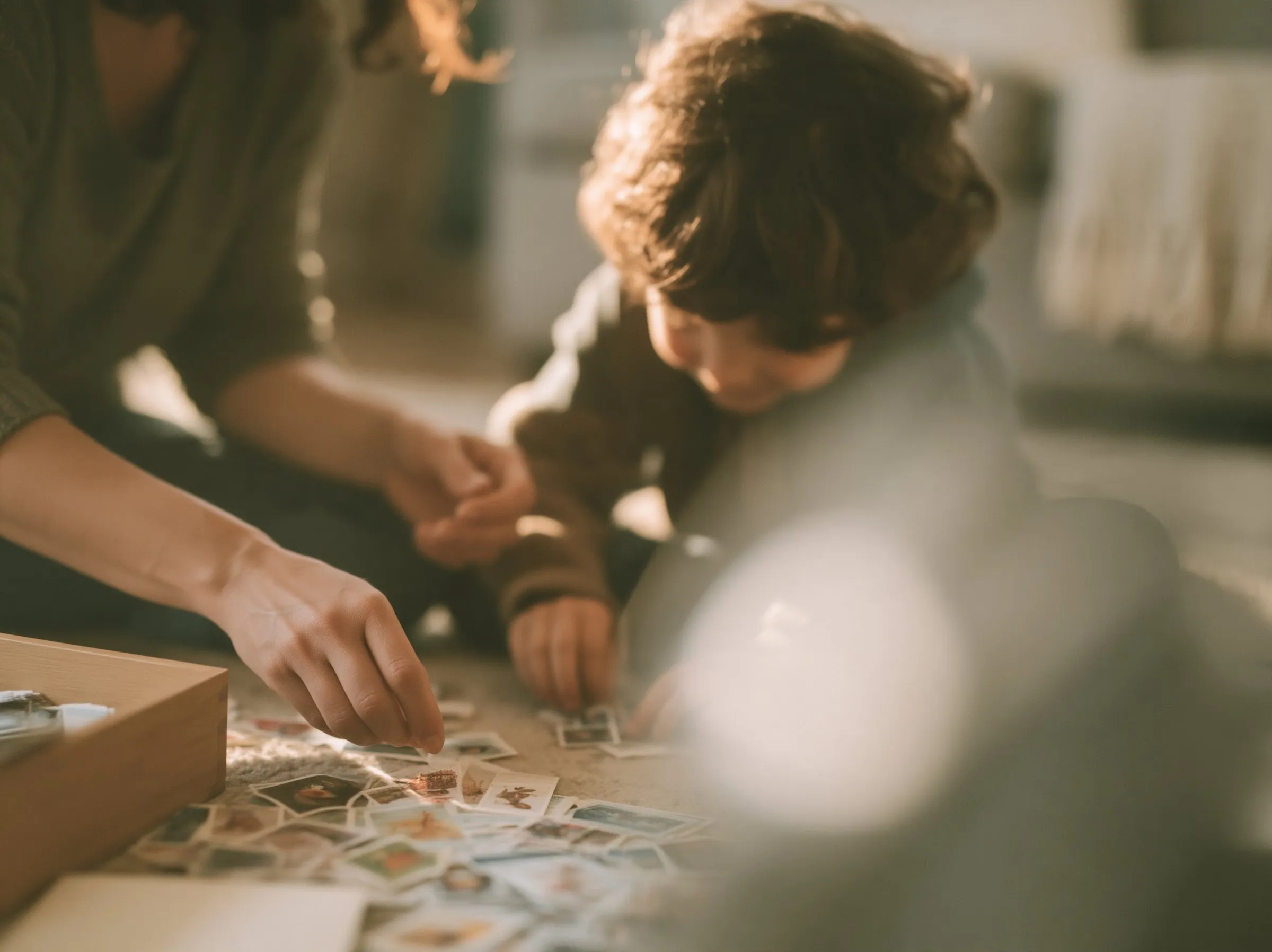 A parent and child on the floor in warm light, sorting through a box of stamps together.